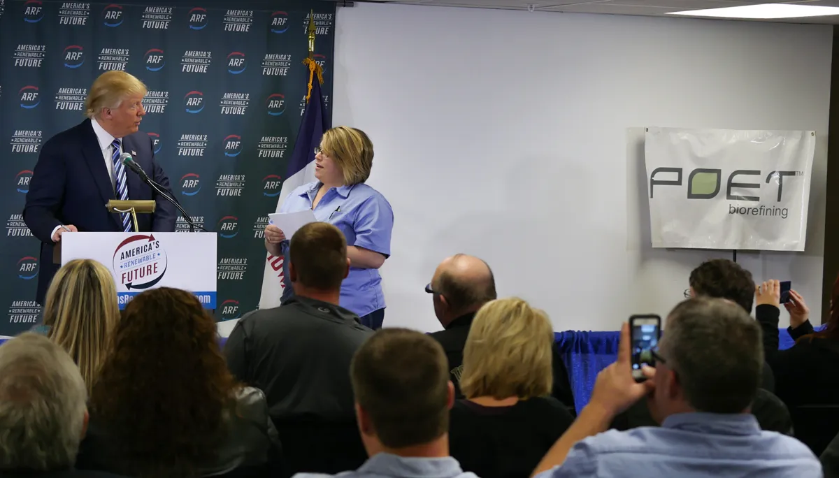 A man in a suit speaks at podium beside a woman in scrubs; ARF banners read America's Renewable Future as audience films.