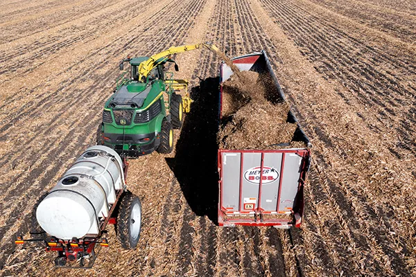 Green tractor with loader dumping into red trailer