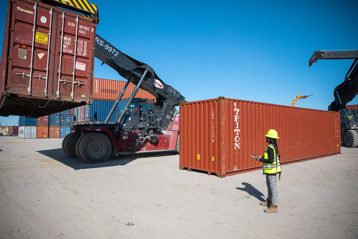 Worker oversees red shipping container move.