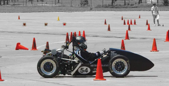 Rider on vintage racing motorcycle amid cones.