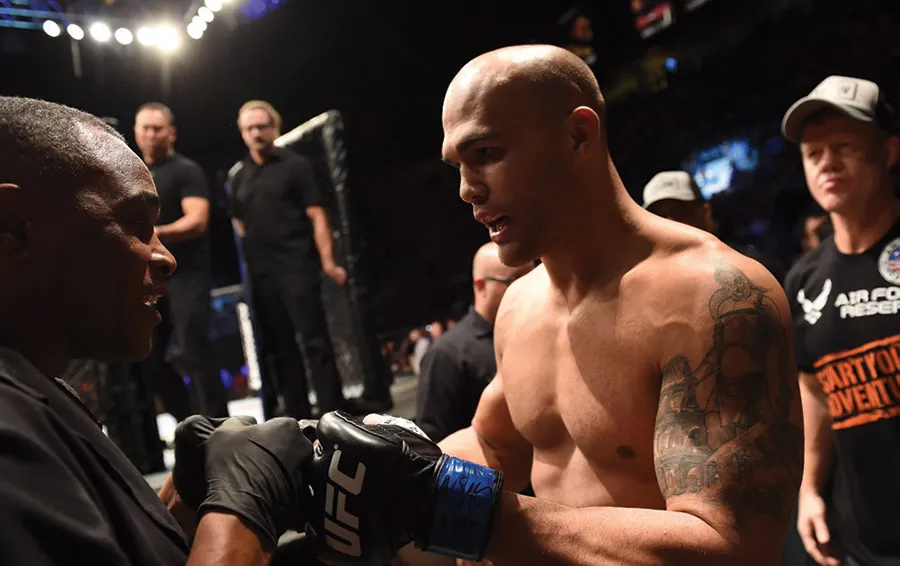 Shirtless fighter with tattoo shakes gloved hand.