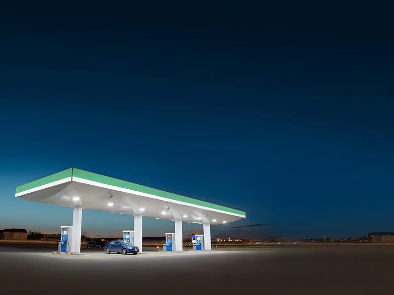 Gas station canopy over pumps and car at dusk.