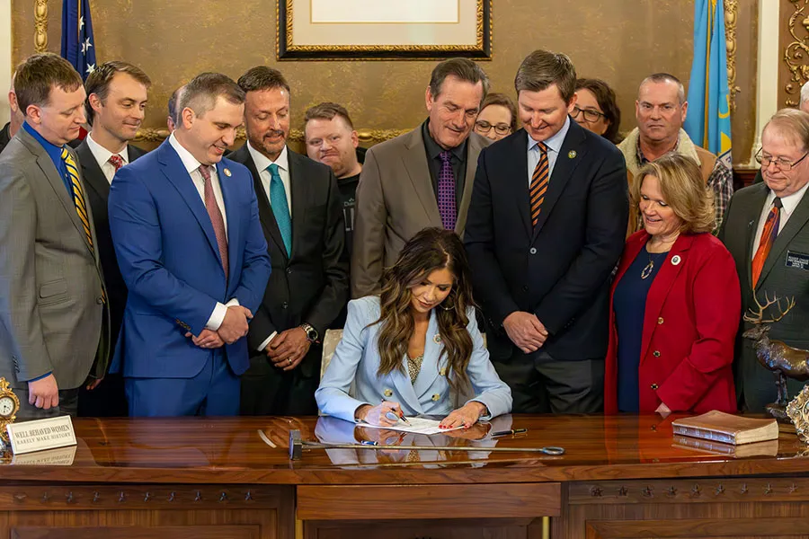 Woman signs document as onlookers watch.