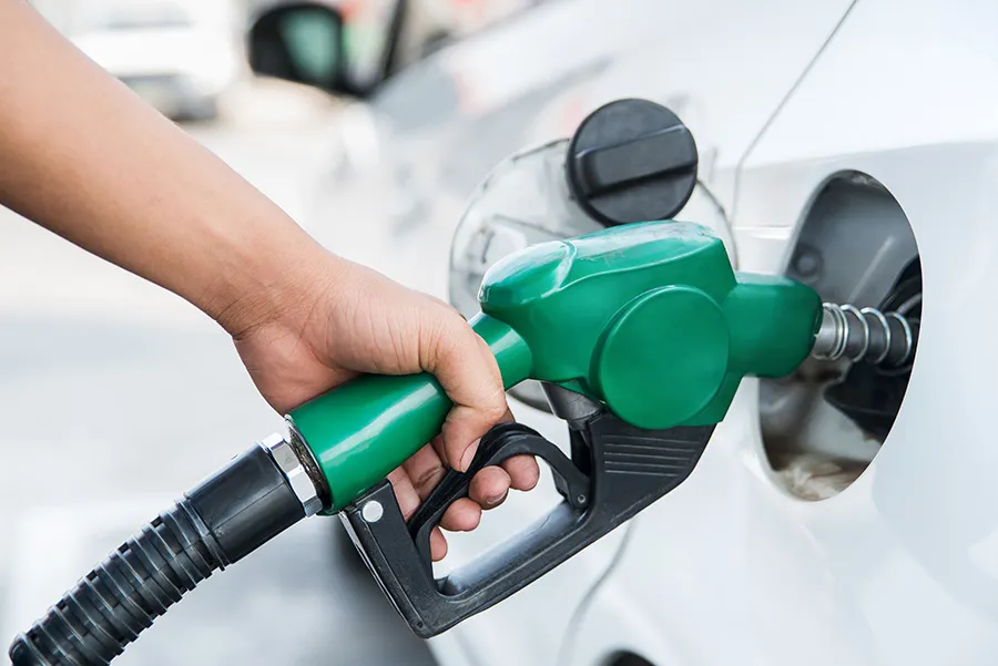 A hand grips a green gas nozzle fueling car.