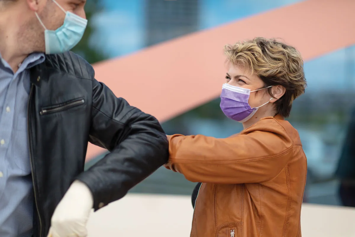 Masked woman elbow-bumps man outdoors