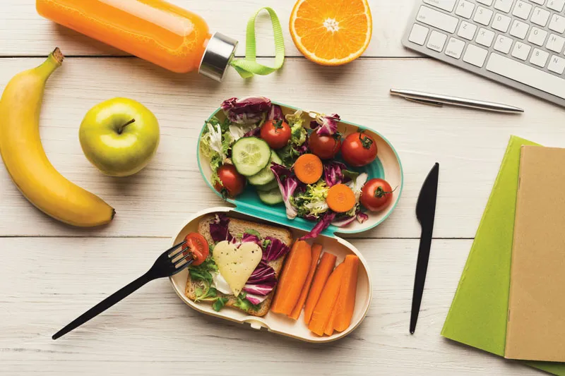 Lunchbox with salad and carrot sticks on desk