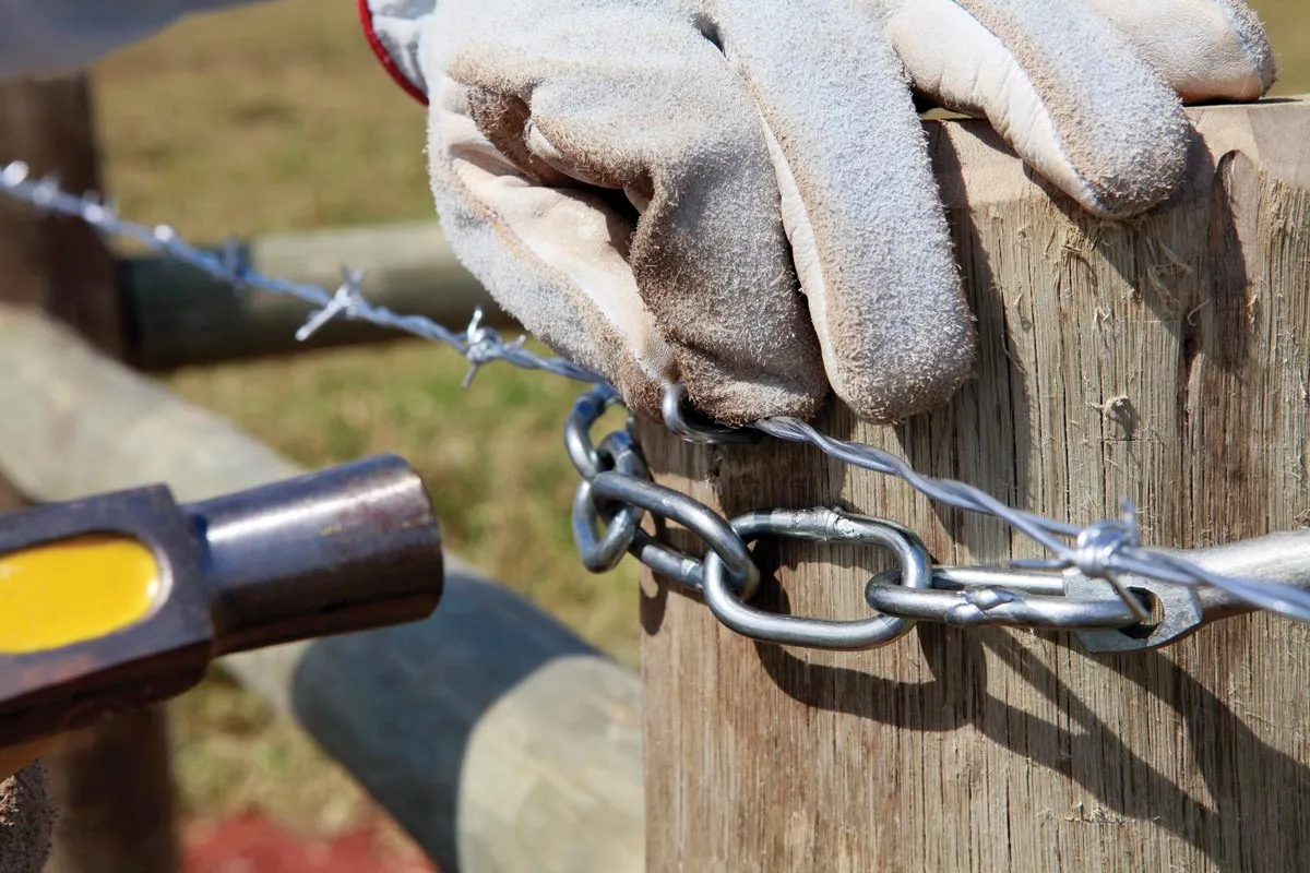 Gloved hands on fence post with barbed wire.