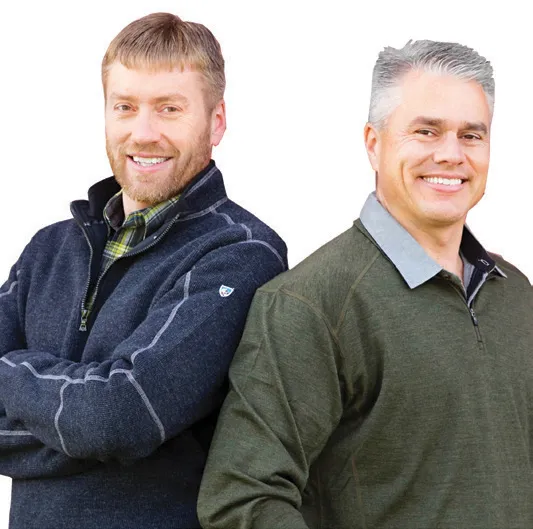 Two men standing back-to-back in casual sweaters.