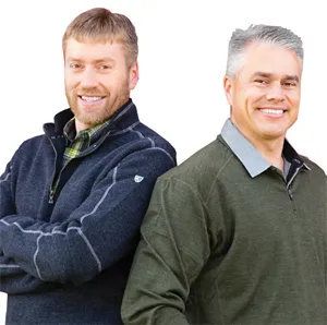 Two men in sweaters stand back-to-back.