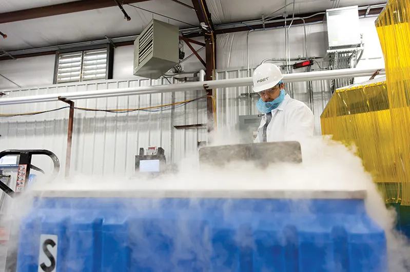 Worker in hard hat and lab coat by blue container
