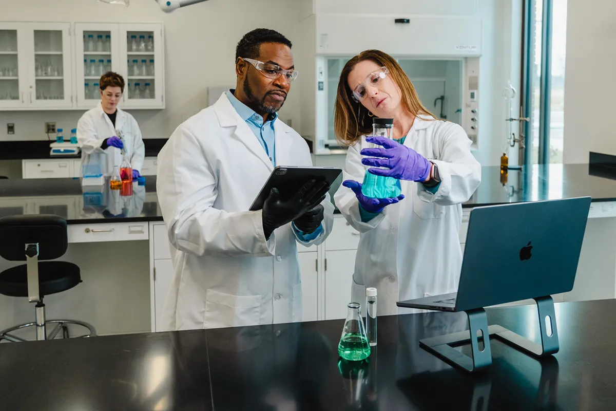 Two scientists examine blue liquid in lab