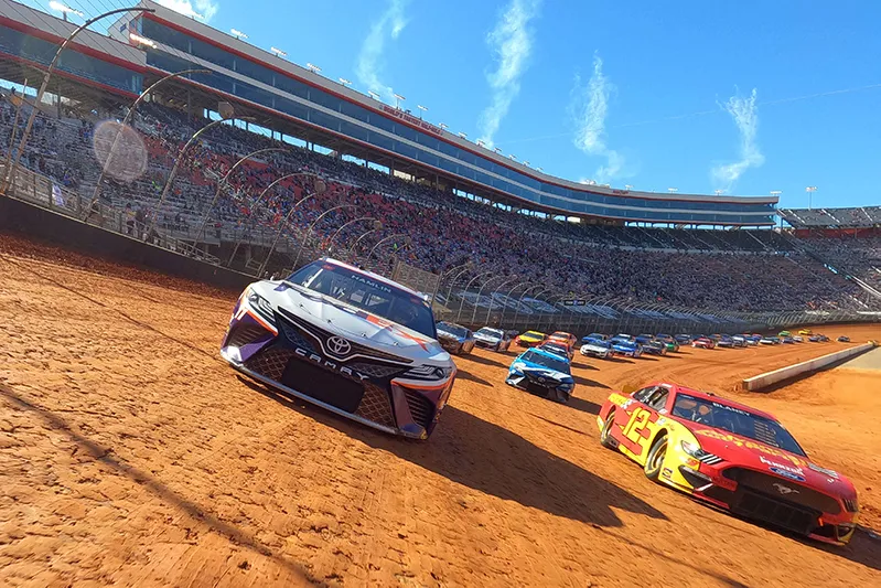 Dirt-track stock cars race past crowded stands