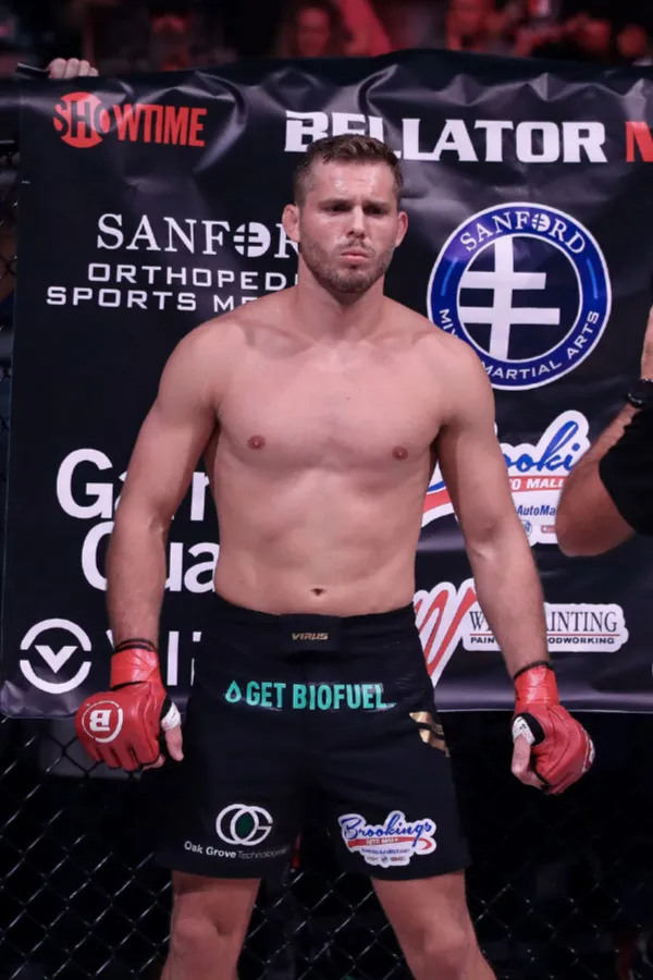 Logan stands in a cage wearing red gloves.