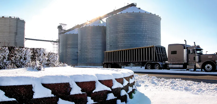 Snowy yard near grain silos and a truck.
