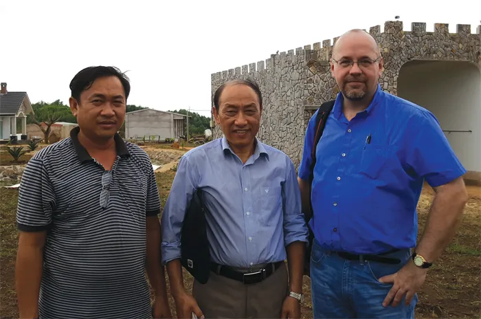 Three men posing outdoors near a stone wall