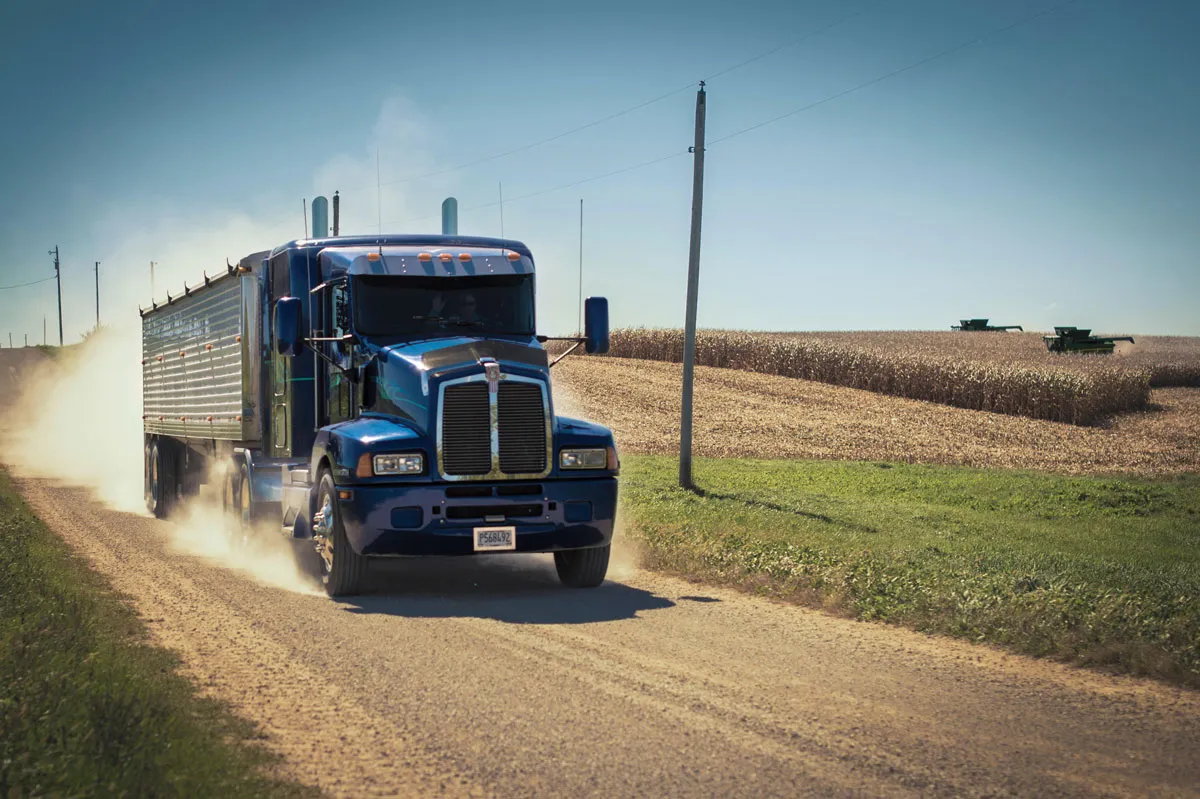 Dark blue truck driving on a road through a corn farm