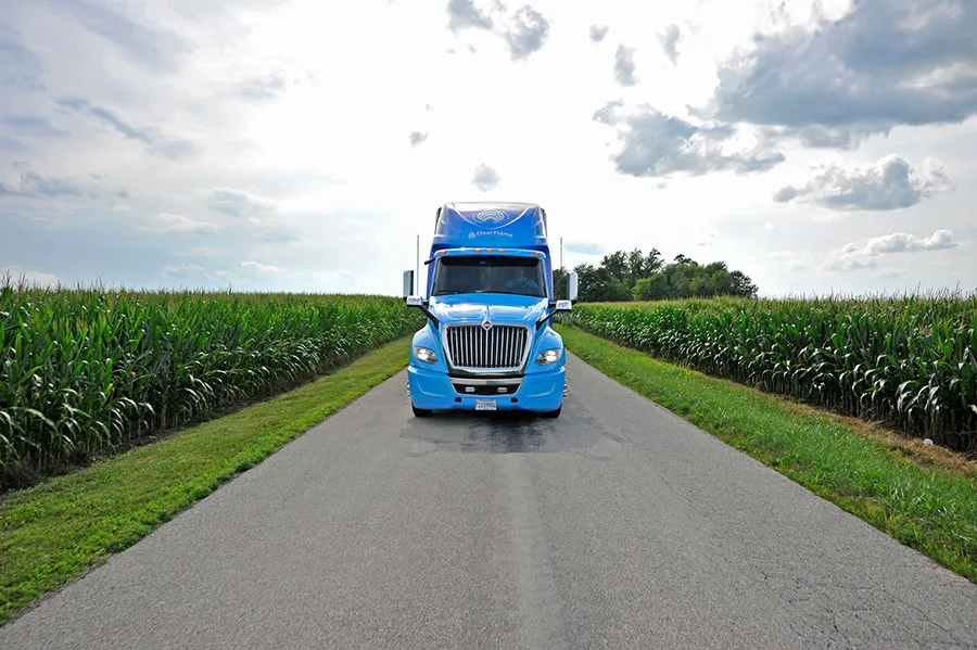 Blue semi-truck travels a rural cornfield road