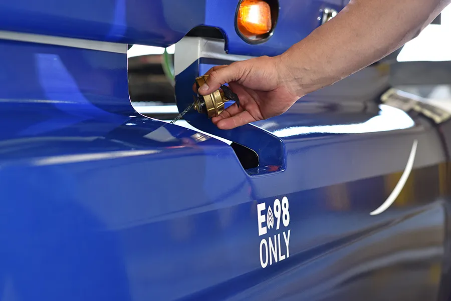A hand unscrews a fuel cap on a blue vehicle