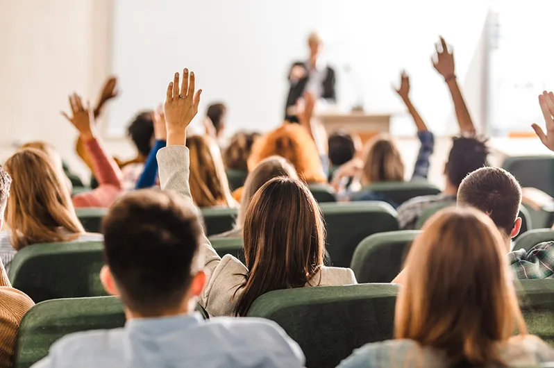 Students raising her hands in a classroom