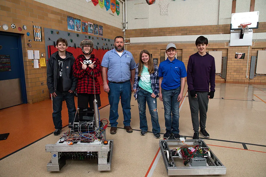 Students and teacher pose with two robots in gym