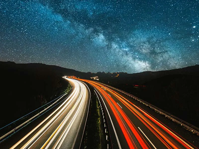 Milky Way over winding highway with light trails