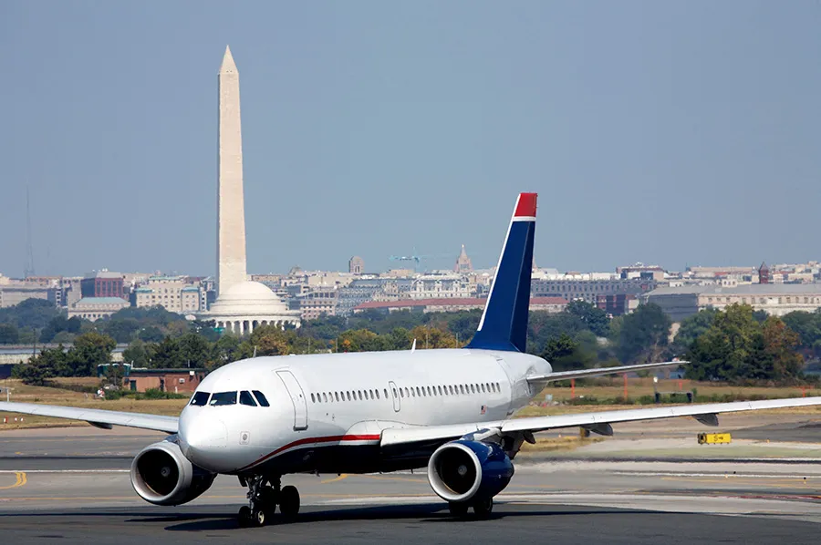 Commercial airplane taxiing on runway with Washington Monument and city skyline in the background.