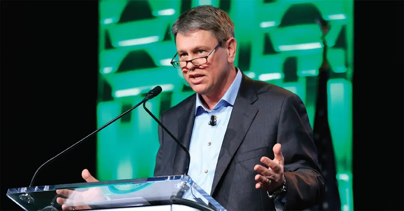 Man in suit speaks at podium on stage