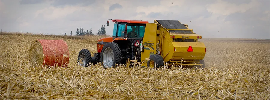 Tractor with yellow baler beside round hay bale