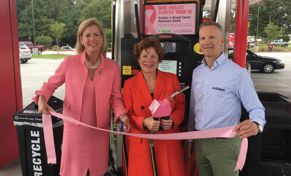 Three people cut pink ribbon at gas station