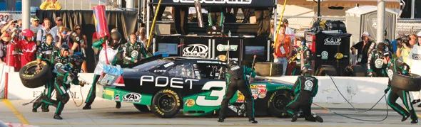 Pit stop with crew servicing green No. 3 race car.