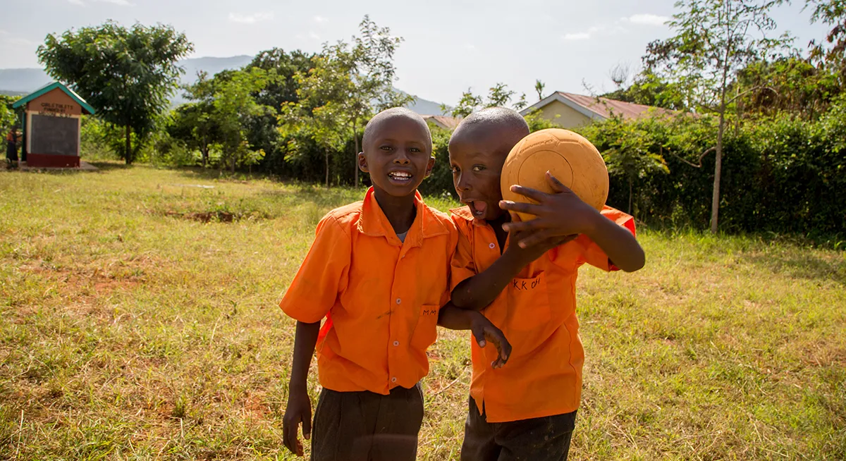 Two kids standing outside while one holding a ball