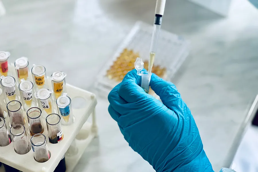 Blue-gloved hand pipetting into a tube