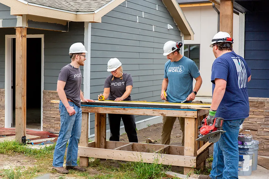 four workers wearing helmet measures wood on site