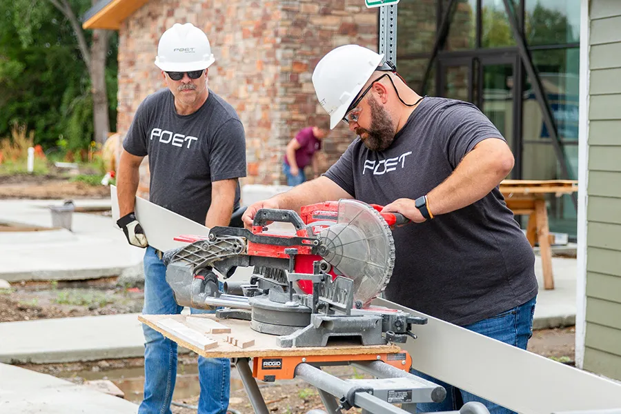 Two workers cutting wood with a miter saw