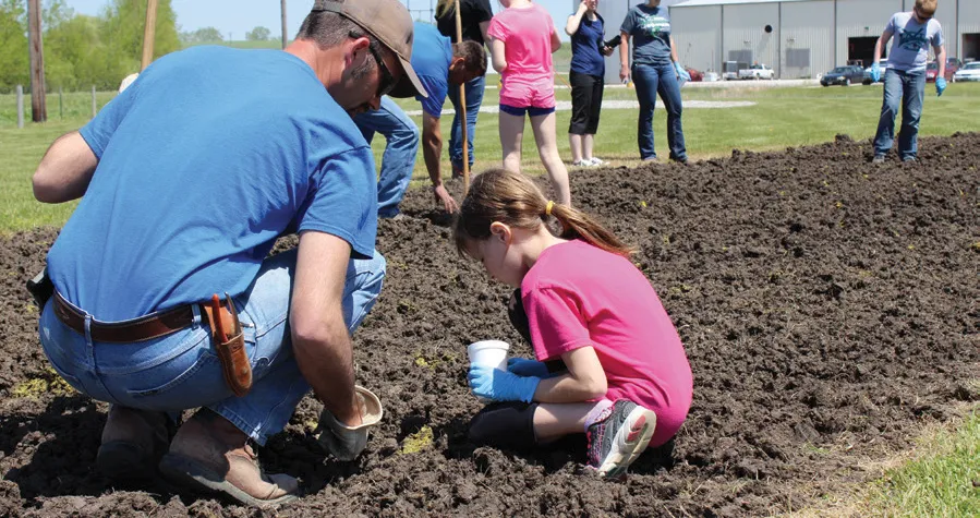Man and girl planting seeds in dirt patch