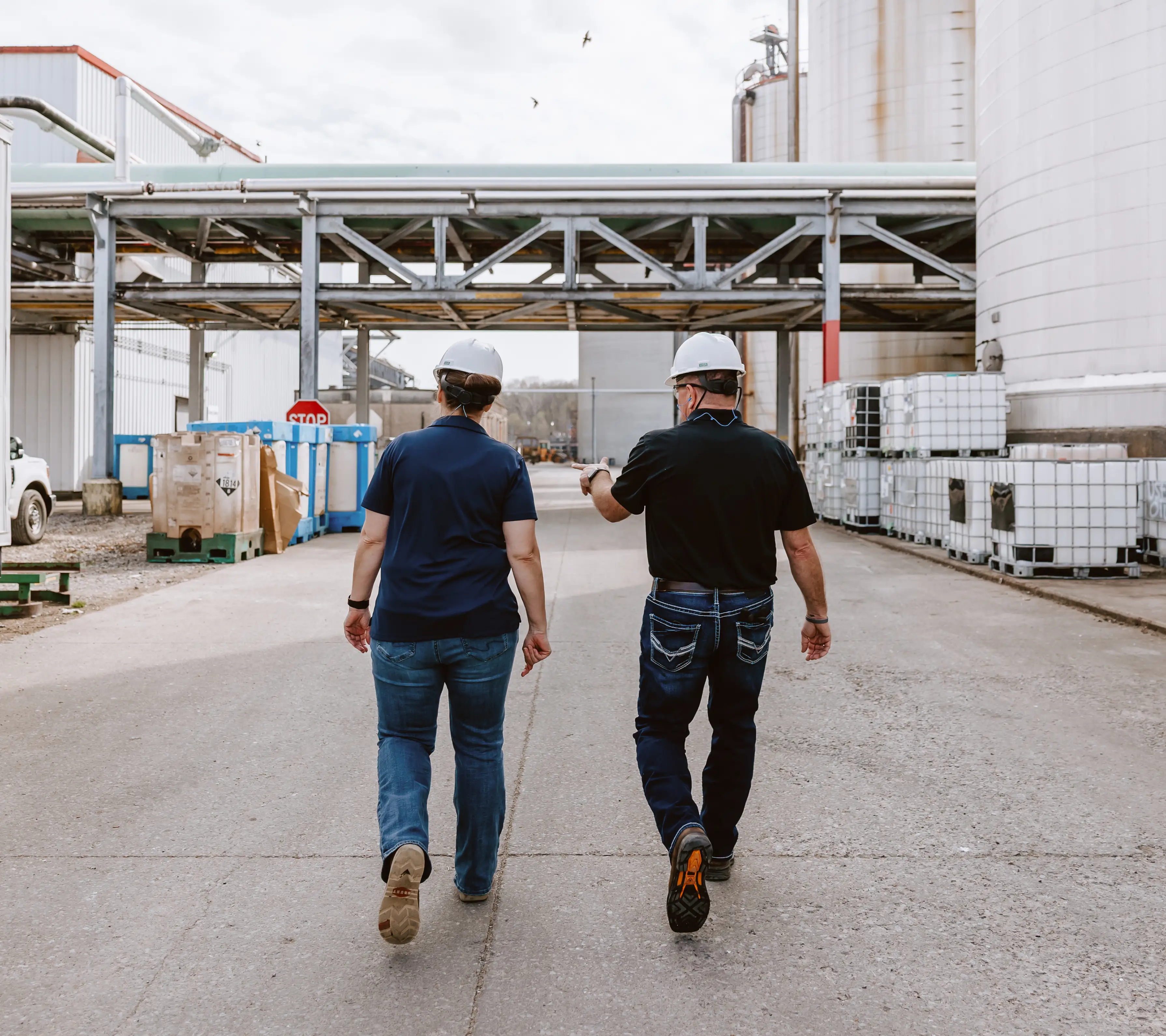 Two POET employees wearing hard hats walking through a bioprocessing site with large white tanks and containers.