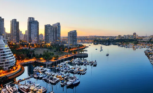 Marina with docked boats and yachts next to a city skyline at sunset.