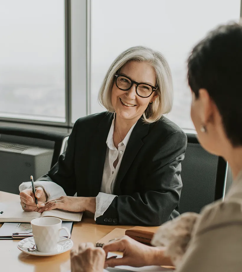 Smiling businesswoman in glasses taking notes during a meeting with a colleague.