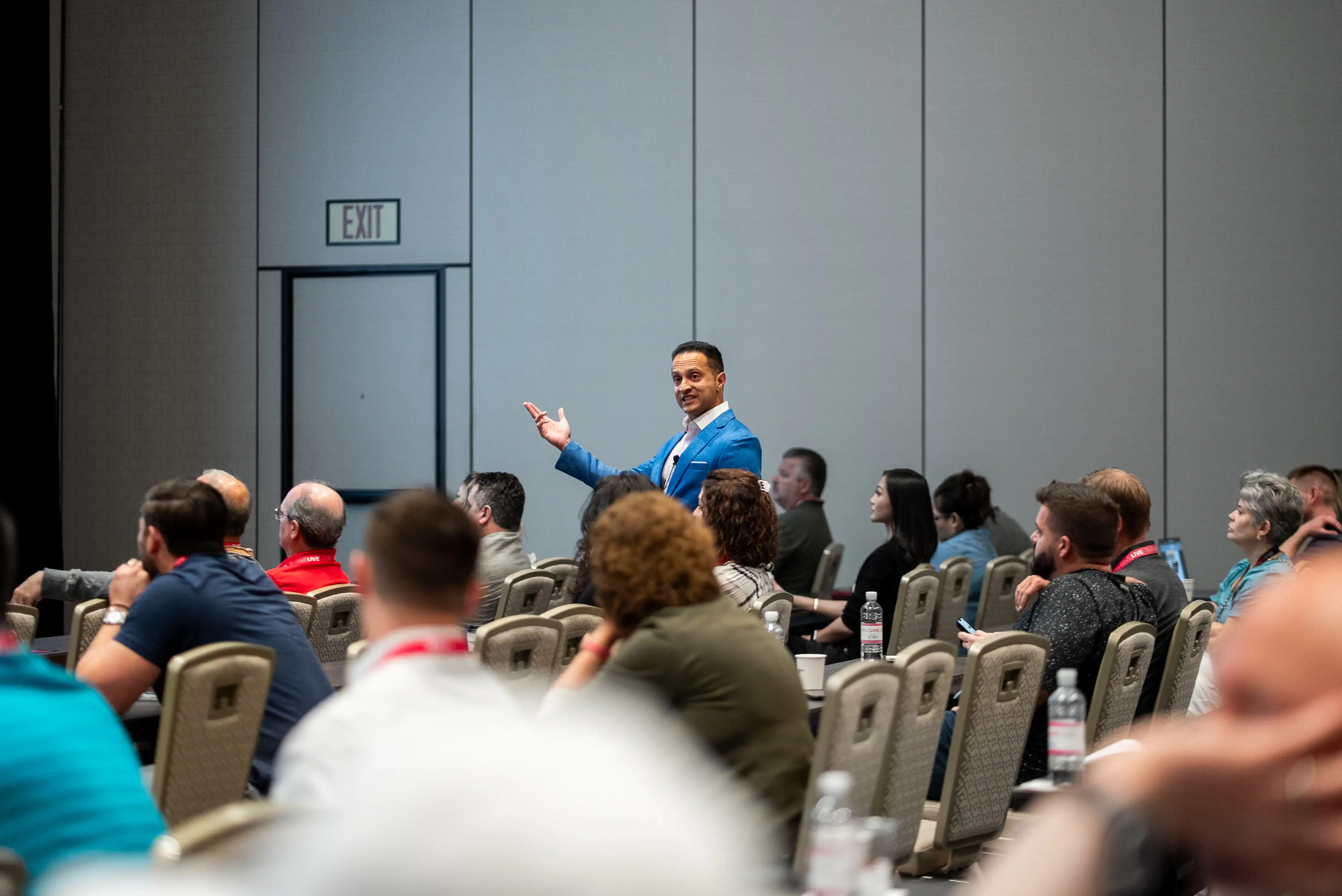 Man in blue blazer speaking to an audience seated in rows inside a conference room.