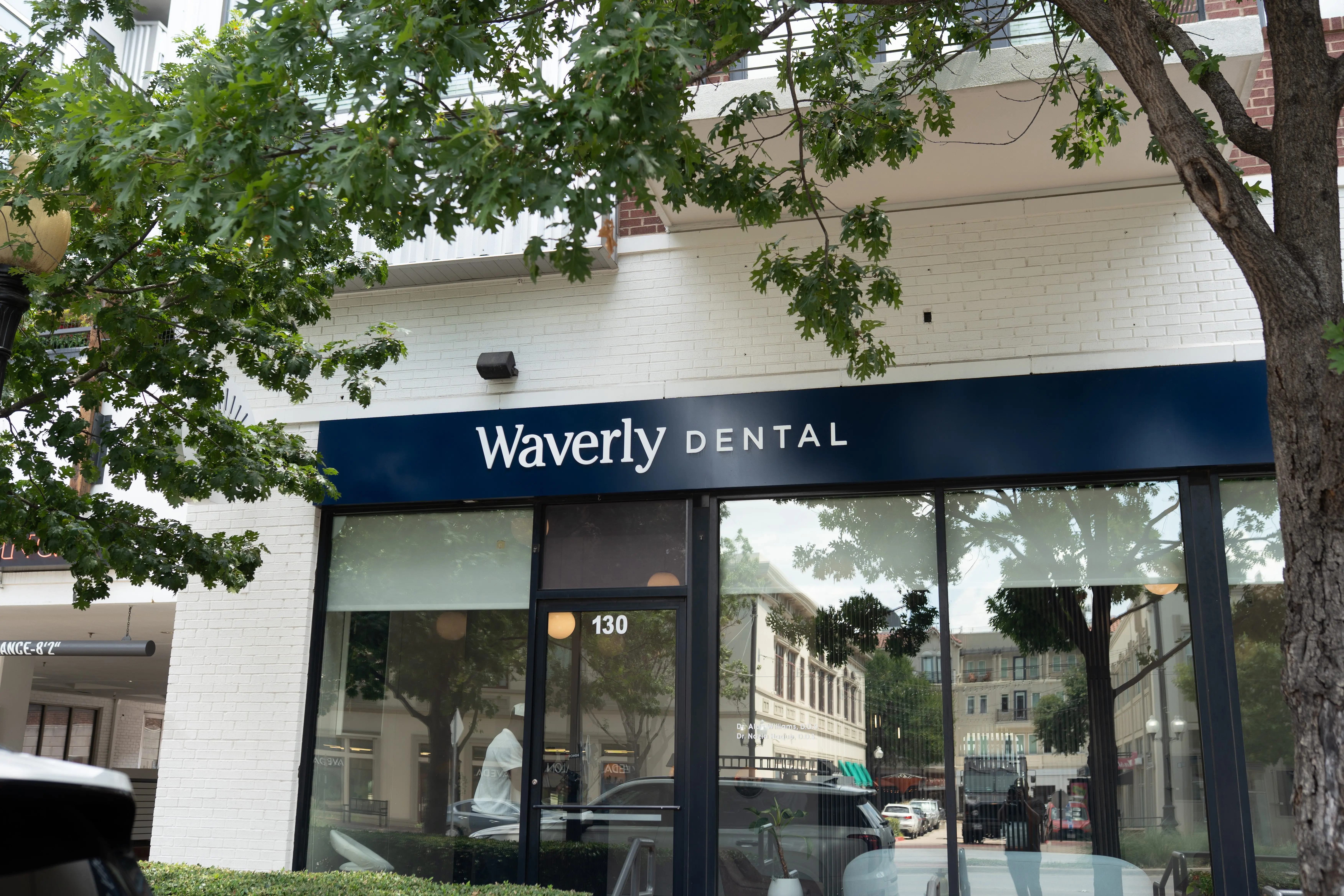 Street-level view of Waverly Dental office with glass doors and windows reflecting nearby buildings and trees.