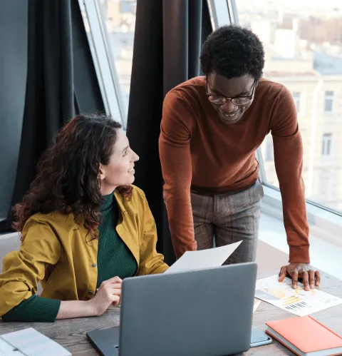 Two people sitting at a table looking at a laptop.