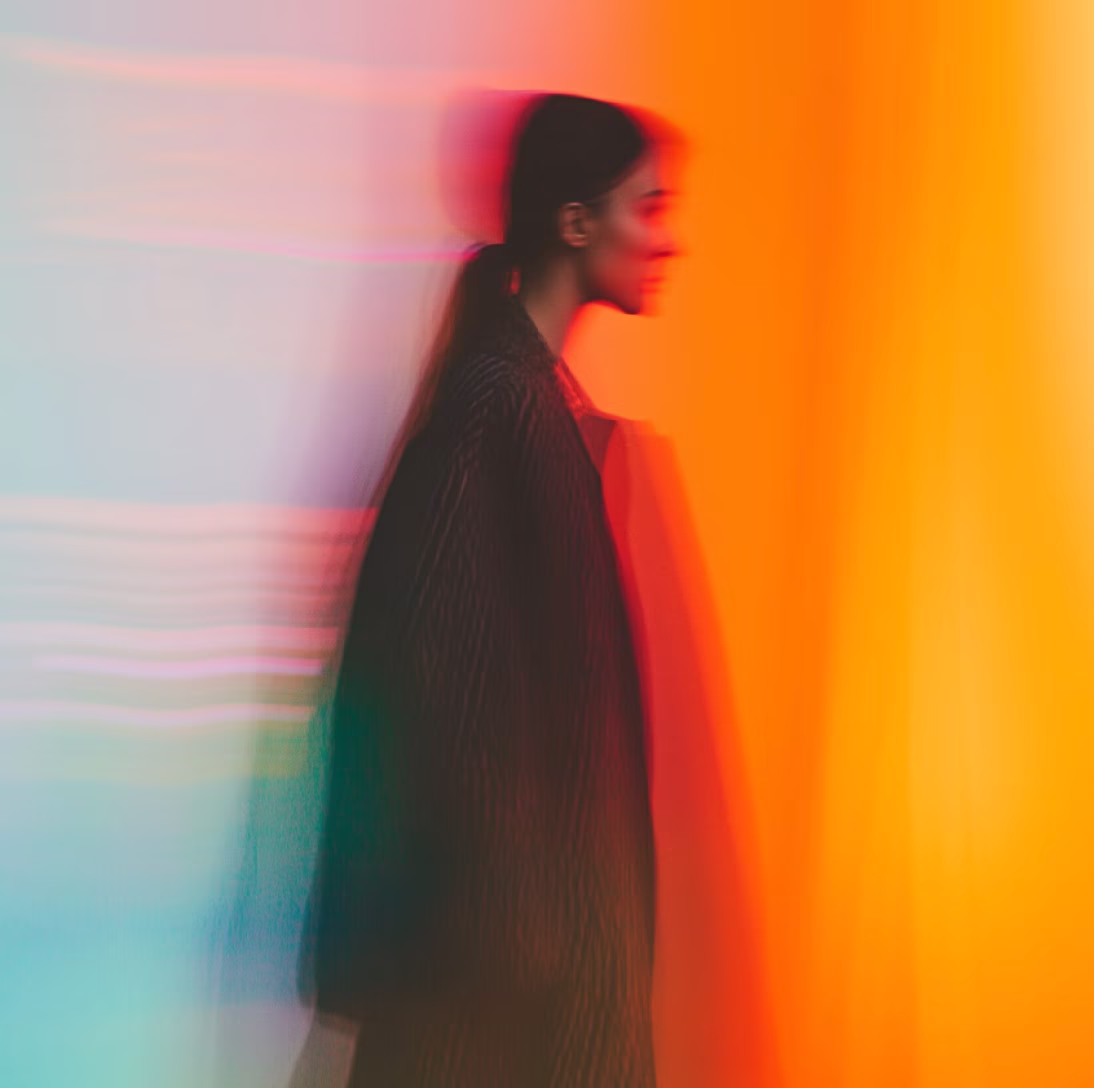 Blurred side profile of a person with a ponytail against a background transitioning from light blue to bright orange.