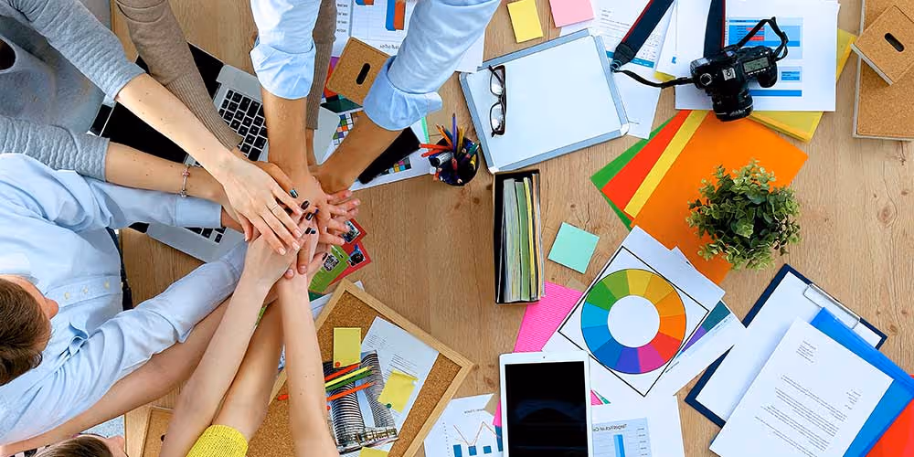 Team bringing hands together over desk