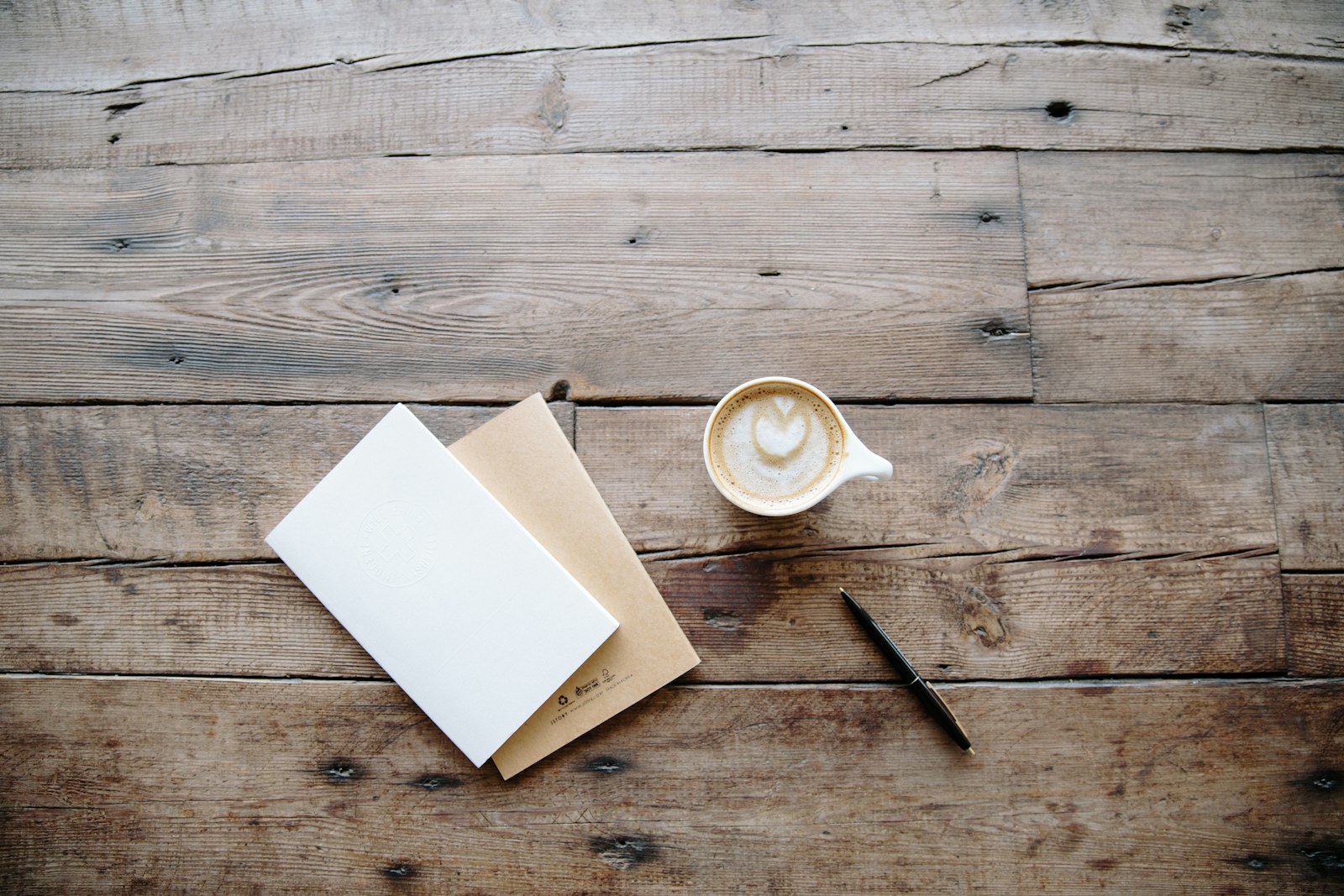 Blank note cards, a pen and a latte on a rustic wooden table