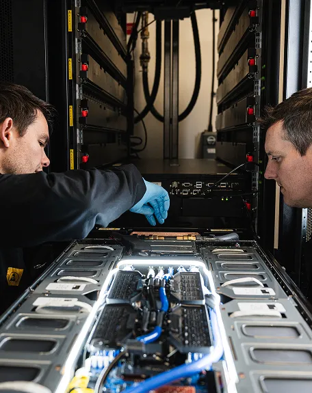 Two technicians working on a server rack inside a data center with illuminated hardware components and cables.