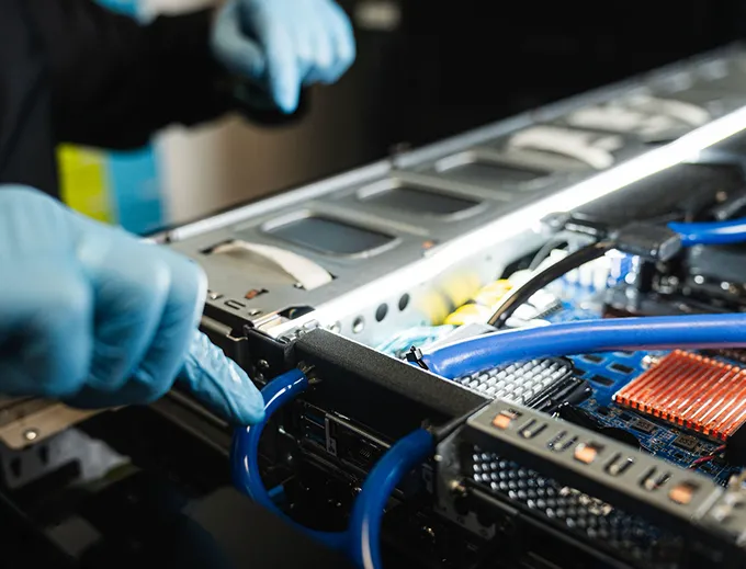 Person wearing blue gloves working on a computer server with visible circuit board and blue cables.