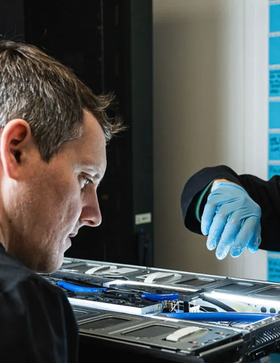 Two technicians working on a server with one wearing blue gloves and focusing on internal components.