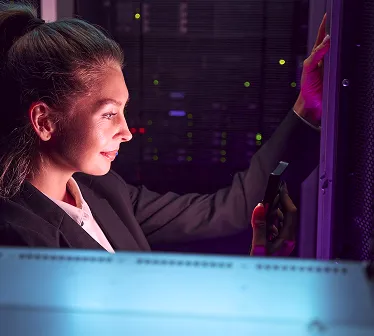 Woman working on a server rack in a dimly lit data center with colorful indicator lights.