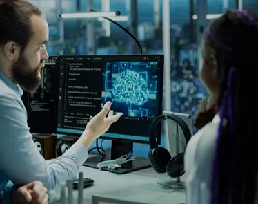 Two people discussing a digital brain image displayed on a computer monitor in a modern office setting.