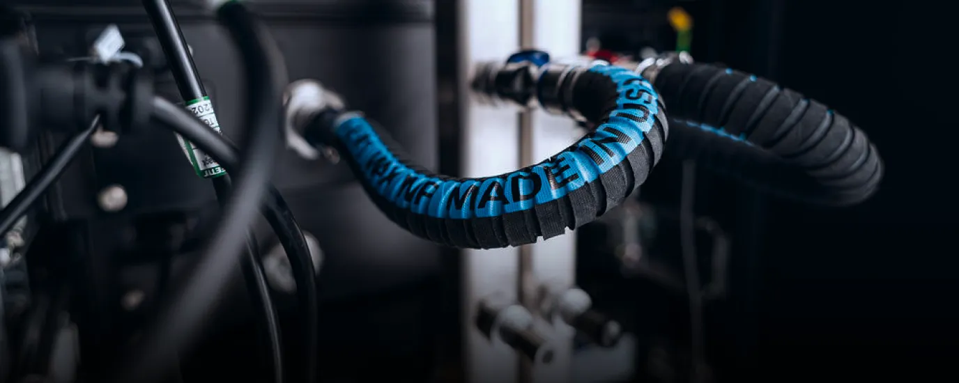 Black flexible industrial cable with blue text wrapped around a machine part.
